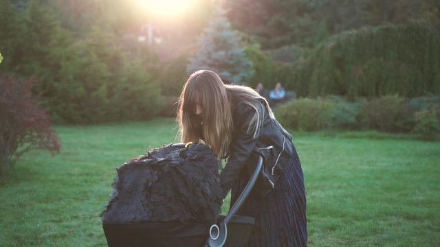 A young mother in a black jacket looks at her child in a baby stroller