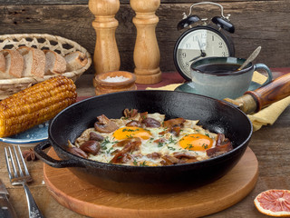 Fried eggs with mushrooms and bacon.Fried corn.On a black iron pan.On wooden background