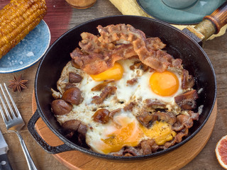 Fried eggs with mushrooms and bacon.Fried corn.On a black iron pan.On wooden background