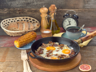 Fried eggs with mushrooms and bacon.Fried corn.On a black iron pan.On wooden background