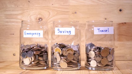 Woman drop coin in the bottle glass to save money for travel on wood background (Thai currency, THB coin)
