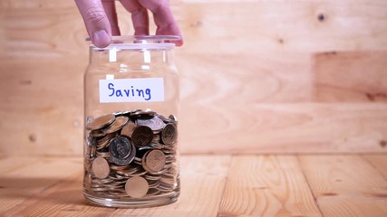 Woman drop coin in the bottle glass to save money for travel on wood background (Thai currency, THB coin)