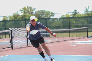 A senior man hits a shot while competing in a pickleball tournament