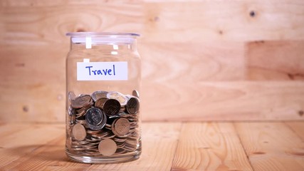 Woman drop coin in the bottle glass to save money for travel on wood background (Thai currency, THB coin)