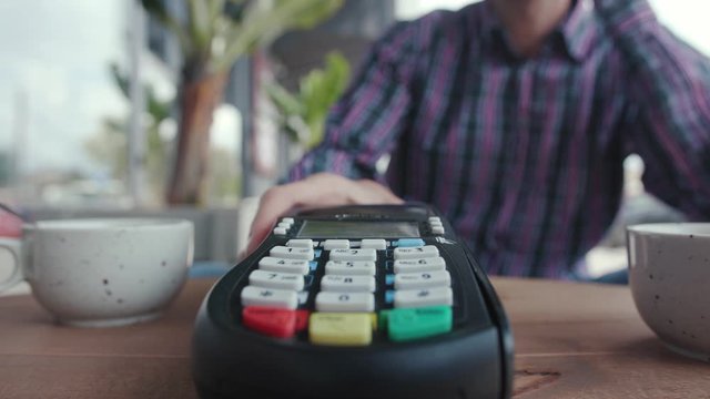 Subjective view of young man customer making payment with credit card entering pin code paying for order inside the cafe.