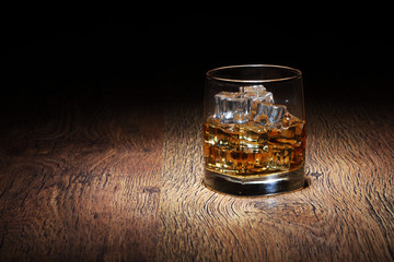 Scotch in glass tumbler with ice rocks on old wood surface