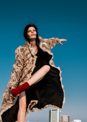 Portrait of brunette girl with short disheveled hair and fashion clothes pose on hill with view of city. Strong wind on hair.