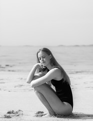 Fototapeta na wymiar Black and white photo of young beautiful girl posing on a beach with sand in black swimwear. Calm, chilling mood of summer.