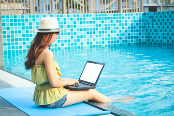 Beautiful woman sitting by the pool She is typing on a laptop computer.