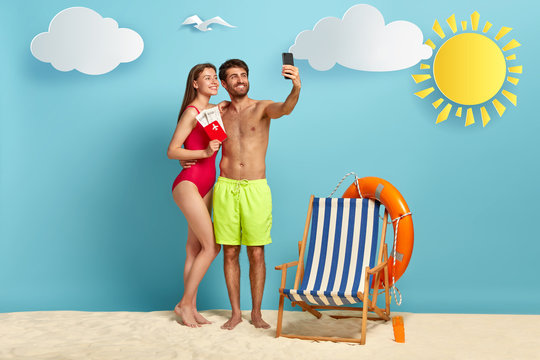 European couple takes selfie on cell phone, pose on beach with passport and flying tickets, rejoice successful traveling, focused in smartphone camera, have summer vacation, make travel photos