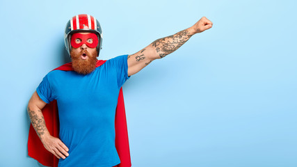 Stupefied emotive man with ginger beard being cartoon character, keeps arm in flying gesture, wears...