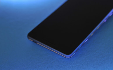 Black touch phone on blue background in neon light.