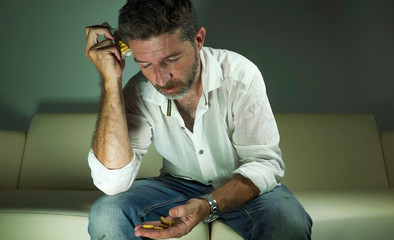 dramatic portrait of young attractive depressed and wasted pills addict man holding antidepressant tablets bottle sitting on couch in drug addiction concept