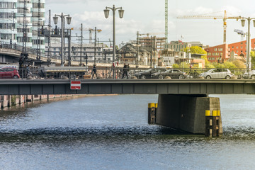 BERLIN, GERMANY - September 26, 2018: Busy urban environment with cars, trucks and people crossing a bridge over the Spree river canal, with buildings under reform and a tower crane in the background