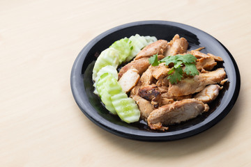 Partially sliced grilled chicken breast with cucumber in black plate on wooden table.