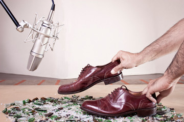 Step Foley over broken glass. Caucassian male hands moving male dress shoes on broken glass near to a silver professional studio mic.