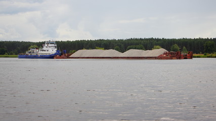 Fototapeta na wymiar Pusher tug boat carries a loaded barge cargo ship with gravel on the river, logistics of cargo transportation by water transport