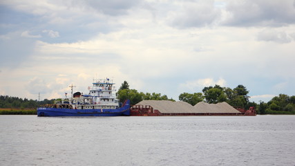 Obraz premium Tugboat vessel carries a loaded barge cargo ship with gravel on the river, logistics of cargo transportation by water transport