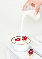 Pouring milk to Healthy breakfast bowl red Cherry Muesli by hand on white background