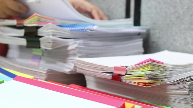 Education and business concept. Asian teacher hands is searching for student's homework assignments archive with colorful papers on table to make a check and inspect. Stack of paperwork and reports. 