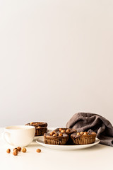 Homemade chocolate cupcakes with glazing, walnuts and a cup of coffee on white table front view