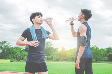 Two young man drinking water from bottle after run. Two young man with bottles of cold drink outdoors