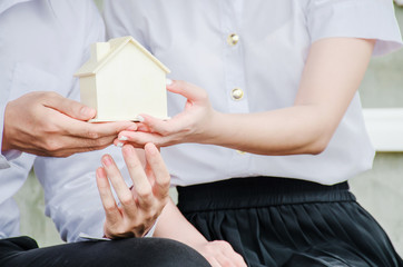 Closeup hands of an couple students holding a little house together, Concept of sustaining a house between two people. Helping your partner in owning a house.