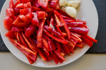Slices of fresh red hot chili peppers and tomatoes with garlic on white plate, close-up