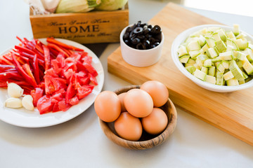 Plates with sliced vegetables and eggs with olives in bowls on kitchen table, cooking process concept