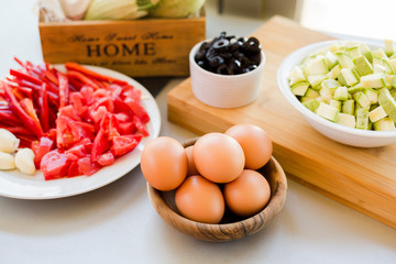 Plates with sliced vegetables and eggs with olives in bowls on kitchen table, cooking process concept