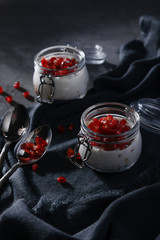 A healthy breakfast in jars of yogurt, oatmeal and pomegranate. Breakfast in a rustic style on a dark background.