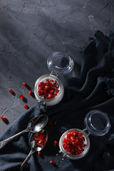 A healthy breakfast in jars of yogurt, oatmeal and pomegranate. Breakfast in a rustic style on a dark background.