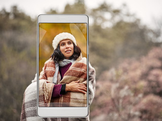 Photo of young woman basking with plaid in autumn park, demonstration of device capabilities