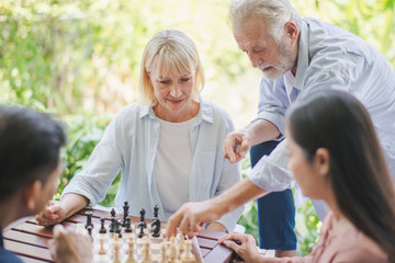 Group of positive seniors European and Asia are playing chess game on the table outdoor at retirement home. Retired people are playing chess having fun to enjoying and smiling felling happy.