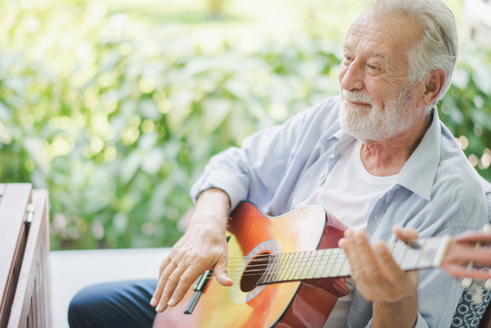 Seniors European man are playing a guitar at outdoor green garden in retirement home. Retired man hare playing a guitar and smiling with felling happy.