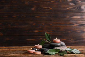 Composition of spa stones, green leaves and burning candles on wooden table, space for text