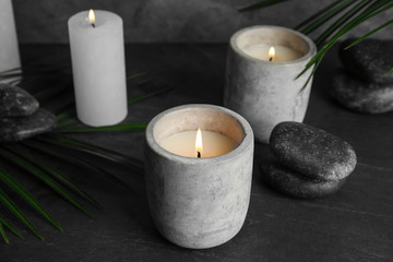 Fototapeta na wymiar Burning candles, spa stones and palm leaf on dark grey table