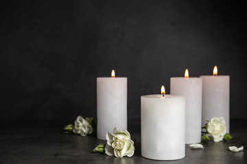 Fototapeta na wymiar Burning candles and beautiful flowers on grey table, space for text