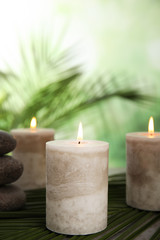Obraz na płótnie Canvas Burning candles and spa stones with palm leaf on table against blurred green background, space for text