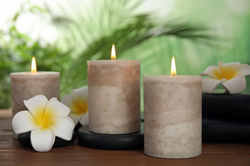 Obraz na płótnie Canvas Burning candles and plumeria flowers on wooden table against blurred green background