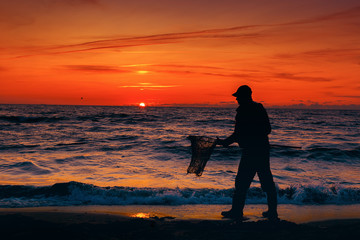 Sunset at the Baltic Sea. Landscape with silhouette. Man on the beach catch amber in the waves