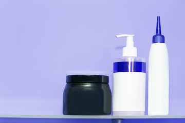 Three bottles of shampoo or shower gel, cream dispenser on colored background with copy space.