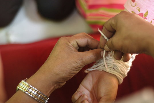 Close-up image of Wrist tying with the ceremonial thread.tying a white sacred thread on the wrist of a newlywed couple in a rural Thai wedding ceremony.