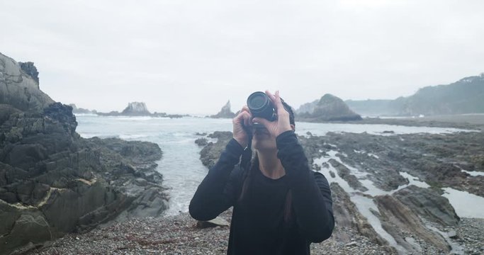 Girl with braids takes photos with her camera on a rocky beach early in the morning. Rocks in the background during low tide. Northern Spain Galicia.