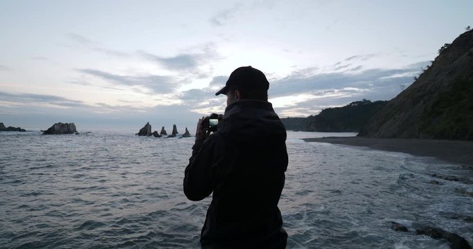 Female photographer waits for the sunrise on the north shore of Spain in Galicia. Dolly like shot.