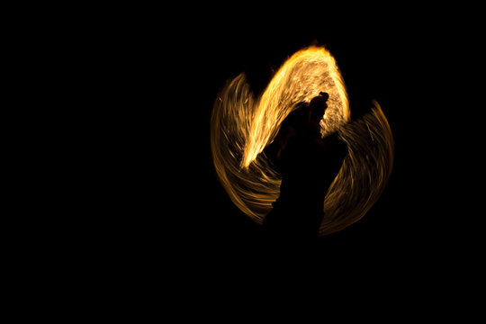 Motion blurred night shot showing a fire eater juggler's torches. Background is dark and blurred, only fire is clearly visible.