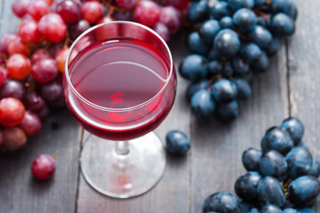 glass of red wine and grapes on black wooden table background