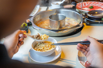 Rear view of young woman eating hotpot with spoon and chopsticks