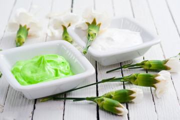 hand and face cream with white carnation flowers on bright wooden table background