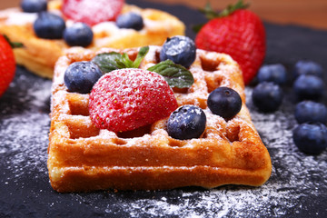 Homemade Traditional belgian waffles with fresh fruit, berries and sugar powder on black plate.